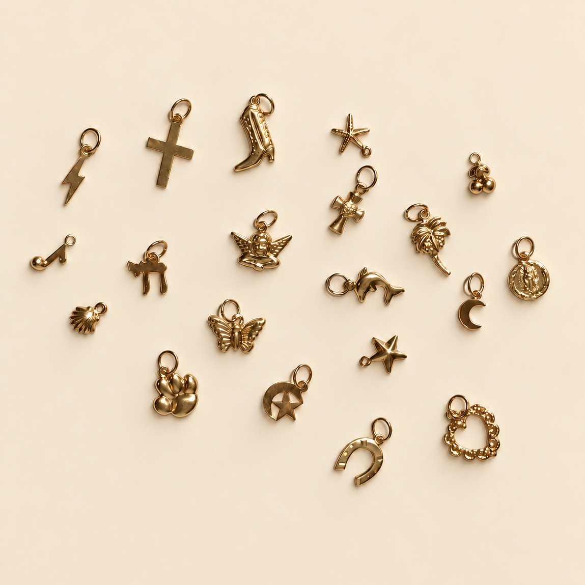 A collection of small 14/20 gold filled charms and pendants arranged on a plain off-white background. The charms include a cross, cowboy boot, lightning bolt, angel, crescent moon, star, horseshoe, wreath, and other symbols.