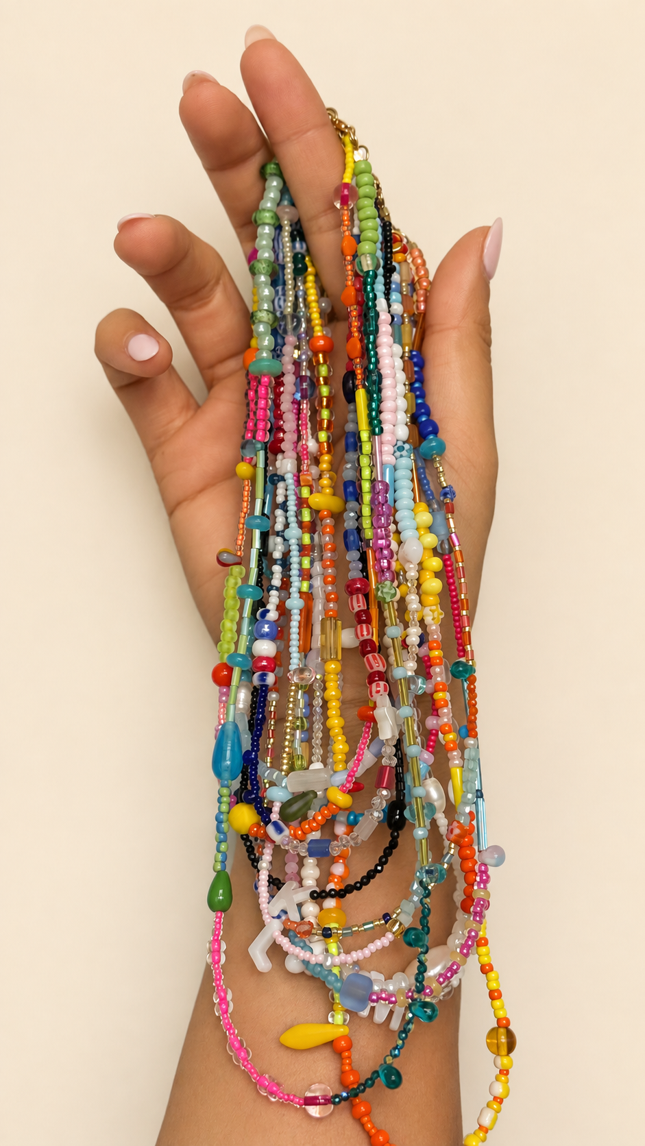 A hand holding a dense bundle of colorful beaded necklaces against a plain light beige background.